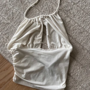 Vit omlott halterneck topp - Säljer en vit halterneck topp med omlott-detalj och öppen rygg. 
