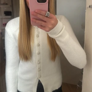 Vit kofta från Zara med pärlknappar - Superfin vit kofta från Zara med långa ärmar och rund hals. Koftan har unika pärlknappar i blomform och är stickad i ett mjukt material. Perfekt för lager-på-lager och ger en clean och söt look.