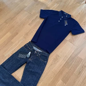 Marinblå pikétröja från Polo Ralph Lauren - Snygg marinblå pikétröja från Polo Ralph Lauren med klassisk krage, tre knappar och broderad vit logga på bröstet. Tröjan är kortärmad och gjord i bomull, perfekt för en clean och stilren look.