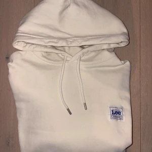 Vit hoodie från Lee med logga - Snygg vit hoodie från Lee med klassisk känguruficka och dragsko i huvan. Tröjan har en broderad Lee-logga på bröstet och är tillverkad i mjuk bomull. Perfekt för en chill och avslappnad stil.