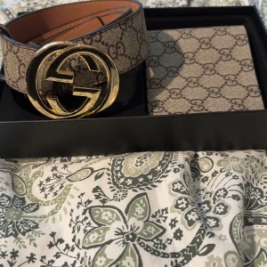 Gucci GG Supreme bälte med guldspänne och Gucci plånbok  - Säljer ett Gucci GG Supreme bälte med klassiskt monogrammönster i beige och brunt. Bältet har ett stort, rundat guldspänne med dubbla G-loggan. Tillverkat i skinn och canvas, perfekt för att lyfta vilken outfit som helst. Plus Gucci plånbok  bältet är 105 cm pris kan diskuteras 
