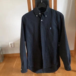 Marinblå skjorta från Ralph Lauren S - Klassisk marinblå skjorta från Ralph Lauren i storlek S. Skjortan har button-down krage, långa ärmar och broderad logga på bröstet. Tillverkad i bomull för en skön och stilren känsla. Perfekt för dig som gillar tidlös och clean stil.