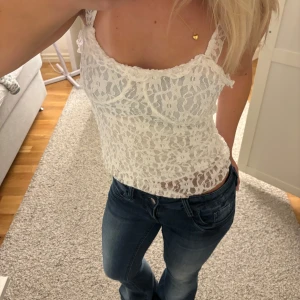 Vit spetsig linnetopp med blommönster - Supersöt vit linnetopp med blommig spets och smala axelband. Toppen är figurnära och har en lätt transparent look som ger en fräsch vibe. Perfekt att styla med jeans eller kjol för en trendig och feminin outfit.