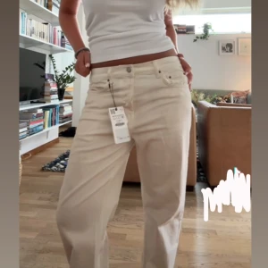 Vita jeans  - Säljer ett par vita/beiga jeans med rak passform och klassisk femficksdesign. Byxorna har hög midja och är tillverkade i bomull. Perfekta för dig som gillar en avslappnad och tidlös look.