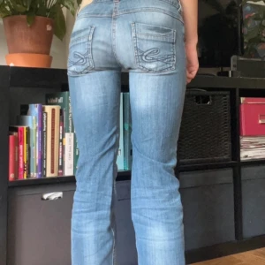 Blåa jeans med slitningar - Säljer ett par ljusblå jeans från esprit med snygga slitningar och broderade bakfickor. Jeansen har låg midja, raka ben och klassisk femficksmodell. Materialet är mjukt jeans i bomull med lite stretch för extra komfort.