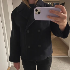 Svart skepparkavaj från Zara - Säljer en svart skepparkavaj från Zara med dubbelknäppning och bred krage. Jackan är i ullblandning, har raka ärmar och två fickor framtill. Perfekt för dig som gillar en klassisk och stilren look med lite boxig passform.