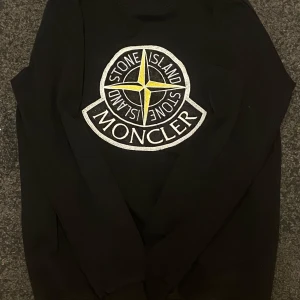 Svart Stone Island sweatshirt med stor logga - Svart sweatshirt från Stone Island med en stor broderad logga framtill i vitt, gult och svart. Tröjan har rund hals och långa ärmar, perfekt för dig som gillar streetwear och vill sticka ut med en fet logga på bröstet.