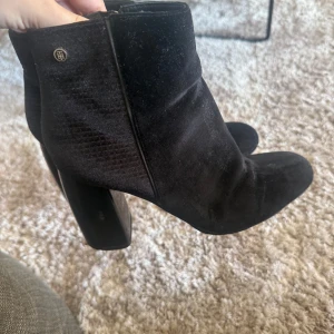Svarta sammetstövletter från Tommy Hilfiger - Snygga svarta stövletter från Tommy Hilfiger i mjuk sammet med rund tå och bred hög klack. Skorna har dragkedja på insidan och diskret logodetalj vid skaftet. Perfekta för dig som vill ha en stilren och trendig look. ÄKTA, nypris 1900 nu säljs för 1000 kr använt ett fåtal gånger, man kan diskutera pris 