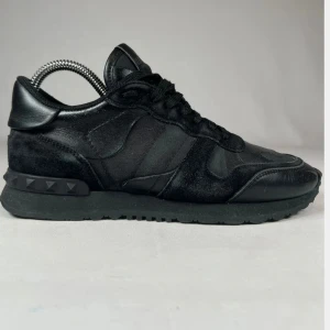 Svarta Valentino Garavani Rockrunner - Snygga helsvarta Valentino Garavani Rockrunner sneakers med coola nitar på hälen. Skorna har en mix av skinn, mocka och textil, samt klassisk snörning. Perfekt för dig som gillar en stilren och lyxig look med streetkänsla.