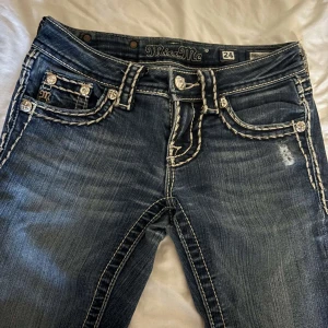 Miss Me jeans Low waist  - Snygga blå Miss Me jeans med tydliga vita kontrastsömmar och dekorativa fickor med broderade detaljer och blanka knappar. Låg midja och bootcut-ben. Köpt för ganska mycket så säljer billigare och pgrund av att dom har fått ett litet hål mellan benen som knappt syns. 