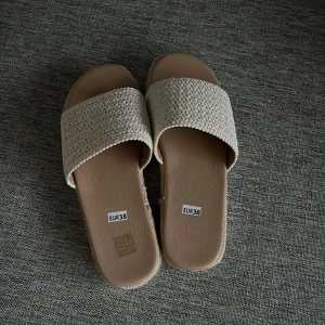 strand sandaler - Snygga beige sandaler med bred flätad rem över foten. Ovandelen är stickad i syntetmaterial och sulan har vit räfflad undersida för extra grepp. Perfekta för sommardagar och ger en chill vibe till din outfit.