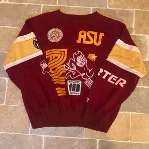 ASU vinröd sweatshirt - Säljer en vinröd och gul sweatshirt från Starter med Arizona State University-tryck och coola patchar fram och bak. Tröjan har långa ärmar med kontrastpaneler och breda muddar. Perfekt för dig som gillar college-stil och sportiga street vibes.