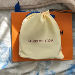 Svart Louis Vuitton skärp i skinn - Exklusivt svart Louis Vuitton bälte i skinn med klassisk LV-logga i mattsvart metall. Bältet har en stilren design och levereras med originalpåse och box. Perfekt accessoar för att lyfta din outfit med en lyxig touch.