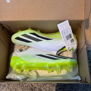 Adidas X Crazyfast elite - Säljer ett par Adidas X Crazyfast.1 LL FG fotbollsskor i vitt och neongult med svarta detaljer. Skorna har en strömlinjeformad design utan snörning och en lätt ovandel i syntetmaterial. Perfekta för dig som vill sticka ut på planen med snabb känsla och grymt grepp.( säljer på grund av att storleken var för liten)