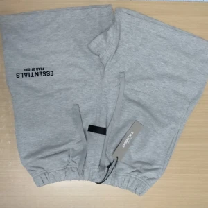 Grå shorts Fear of God Essentials - Snygga grå shorts från Fear of God Essentials med elastisk midja och snörning framtill. Mjuk bomullskvalitet, loose fit och diskret logga på benet. Perfekta för chill dagar och streetwear-stil. Bakficka för extra funktion. Shortsen för 499 egentligen 1000. Både shortsen och tröjan för 799 kr.