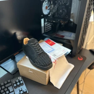 Christian Louboutin. kolla min profil! - Svarta sneakers från Christian Louboutin med ikonisk röd sula och coola svarta nitar på tån. Skorna har snörning och är tillverkade i skinn och mocka för en lyxig känsla. Perfekta för dig som vill sticka ut med en edgy och exklusiv stil. Allt följer med.