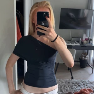 Mörkblå oneshoulder topp - Säljer en mörkblå topp med oneshoulder-design. Toppen är figurnära och har snygga rynkade detaljer längs sidorna.