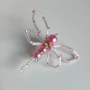 Rosa pärlbrosh i form av fjäril  - Unik brosch formad som en fjäril, gjord av rosa och samt transparenta skimrande pärlor samt tunna metalltrådar. Perfekt för att ge din outfit en söt och lekfull touch eller en söt accessoar till väskan