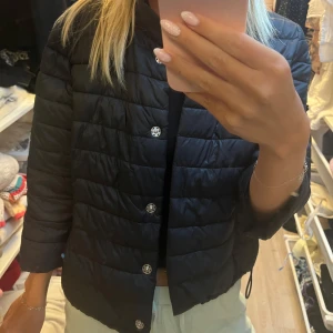 Svart pufferjacka, korta armar!  från Amisu - Säljer en svart kortärmad pufferjacka från Amisu med raka linjer och knappar framtill. Jackan har en enkel, stilren design med lätt vaddering och kortare passform. Perfekt för dig som vill ha en snygg och lätt jacka till vardags.