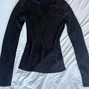 Svart ribbad stickad tröja NA-KD - Svart långärmad stickad tröja från NA-KD i storlek S. Tröjan har en snygg v-ringning och är ribbad för en tightare passform. Perfekt till höst och vinter när du vill ha något stilrent och bekvämt. Den har en liten fläck men den syns knappt!