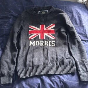Morris stickad tröja  - Snygg stickad tröja från Morris i mörkgrått med Union Jack-flagga och Morris-logga på bröstet. Är i bra skick, tröjan är sällsynt och elegant.