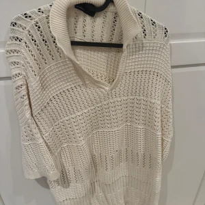 Vit stickad polotröja med v-ringning - Säljer en vit stickad polotröja med bred krage och v-ringning. Tröjan har ett snyggt hålmönster och är tillverkad i mjukt stickat material. Perfekt för dig som gillar en chill och stilren look. Passar både till jeans och kjol.