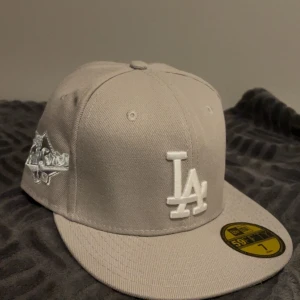 Grå LA Dodgers 59FIFTY keps - Snygg beige 59FIFTY keps från New Era med LA Dodgers broderat i vitt framtill och 1988 World Series patch på sidan. Klassisk flat brim och strukturerad form. Tillverkad i 100% polyester, perfekt för dig som gillar sportig streetstyle. Pris kan diskuteras 