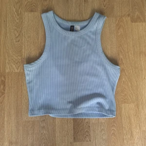 Ljusblå ribbad linnetopp från Divided - Supersnygg ljusblå croppad linnetopp från Divided, perfekt för varma dagar. Toppen är ribbad och har breda axelband med rundad halsringning. Materialet är mjukt och stretchigt, vilket gör den riktigt bekväm att bära.