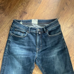 Morris mörkblå jeans slim fit - Snygga mörkblå jeans från Morris med klassisk femficksdesign och diskret logga på myntfickan. Jeansen har slim passform, orange kontrastsömmar och är tillverkade i mjukt bomullstyg med lite stretch för extra komfort pris kan diskuteras .