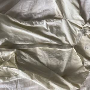 Ljusgul randig skjorta från Bummullsväveri - Snygg ljusgul skjorta från  boomerang med tunna vita ränder. Skjortan har klassisk krage, knäppning framtill och långa ärmar. Tillverkad i mjuk bomull som känns skön mot huden. Perfekt för dig som gillar en clean och fräsch stil. Den är lite missfärgad under armhålorna men syns knappt. Inköpspris: 1199