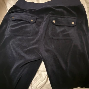 Mörkblå velourbyxor Juicy Couture XS - Mörkblå mjukisbyxor från Juicy Couture i velour med snörning i midjan och stora fickor både fram och bak. Inte använda så mycket därav säljs dom, ända ”felet” är att de saknas en metal sak på ena snöret 