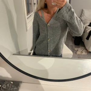 Grå kofta från 157 med knappar - Mysig grå kofta från 157 i storlek XS. Koftan har en v-ringad hals, tre stora knappar framtill och är långärmad. Materialet är stickat och inte alls stickig! Har nästan aldrig använt så den är som ny!