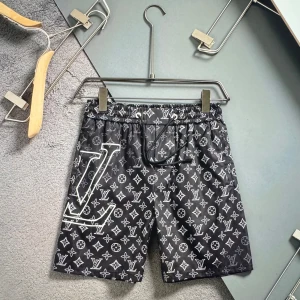 Svarta shorts med logga - Snygga svarta shorts  med ikoniskt monogrammönster i vitt och stor logga på ena benet. De har snörning i midjan och är tillverkade i ett lätt syntetmaterial, perfekta för sommaren. Passar dig som gillar exklusiv streetstyle.