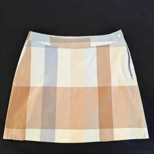 Kortkjol - Säljer en snygg kortkjol från s.Oliver med rutigt mönster i beige, ljusblått och vitt. Kjolen har dragkedja i sidan och knapp i midjan. Tillverkad i bomull, perfekt för en chill och stilren look.