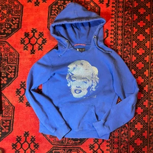 Blå hoodie med tryck från Andy Warhol by Pepe Jeans - Säljer en blå hoodie med ett ikoniskt tryck av Andy Warhol på framsidan. Tröjan har en klassisk huva med dragsko och ribbade muddar vid ärmslut. Perfekt för dig som vill ha en unik och konstnärlig stil.