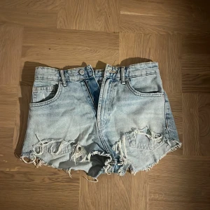 Ljusa jeansshorts med slitningar från Zara - Snygga ljusblå jeansshorts från Zara med och råa, slitna kanter. Shortsen har klassisk femficksdesign och coola slitningar framtill för en avslappnad vibe. Perfekta för sommardagar och festivaler.