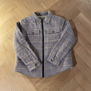 Rutig teddyjacka från Bonpoint 8år - Snygg rutig teddyjacka från Bonpoint med dragkedja och två bröstfickor med knappar. Yttermaterialet är i röd, blå, gul och vit rutig ullmix och insidan är fodrad med mjuk teddy. Perfekt för höst och vinter när du vill vara både varm och stilren. Denna jacka är en fransk 8 så är lite liten i storleken