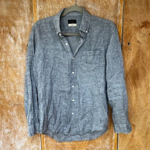 Grå linneskjorta från Prestige Style - Snygg grå skjorta i linne från Prestige Style. Skjortan har klassisk krage, knäppning framtill och en bröstficka. Långärmad och perfekt för en chill och stilren look. Luftigt material som passar bra till varmare dagar.