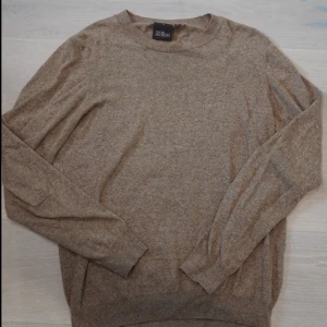 Beige stickad tröja Oscar Jacobson - Snygg beige stickad tröja från Oscar Jacobson, tillverkad i Italien. Tröjan har rund halsringning och långa ärmar, perfekt för dig som gillar stilrena och klassiska plagg. Materialet är mjukt och skönt, passar dig som vill ha en enkel men elegant look.