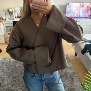 Brun omlott kofta med vida ärmar - Säljer en brun omlott kofta/jacks med breda ärmar.Jackan har en kortare passform. Två knappar som att knäppa med. Storlek 34 och knappt använd. Fint skick! 
