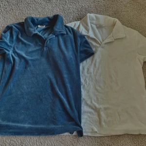 Blå och vit frotté t-shirt med krage - Två t-shirts i frotté, en i mörkblå och en i vit. Båda har klassisk krage och korta ärmar, perfekt för chill dagar. Materialet är mjukt och skönt mot huden. Snyggt retro-vibe och passar dig som gillar enkel stil med twist.