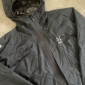 Svart vindjacka från Haglöfs dam M - Svart vindjacka från Haglöfs för dam i storlek M. Jackan har huva, hel dragkedja framtill och diskret logga på bröstet. perfekt för blåsiga dagar. Enkel och stilren design med elastiska ärmslut. Pris kan diskuteras☺️