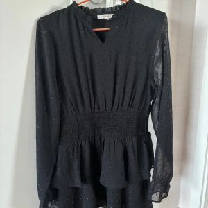 Svart klänning Gina Tricot - Snygg svart kortklänning i storlek 158/164 från Gina Tricot med glittriga prickar, volang nedtill och smock i midjan. I väldigt fint skick och endast använd en gång!🖤