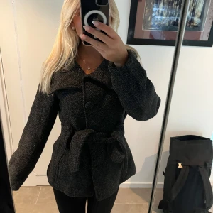 Svart kappa med bälte och stora knappar - Fin jacka nu till hösten, olika knappar och knappen i mitten är borta.. Jag märker inget så ja knyter den där runt midjan så inget man alls tänker på!