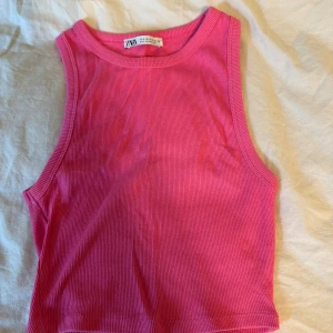 Rosa ribbad linnetopp från Zara - Säljer en snygg rosa ribbad linnetopp från Zara. Toppen är croppad och ärmlös med rund halsringning, perfekt för varma dagar. Enkel och stilren design som är lätt att matcha med jeans eller kjol.