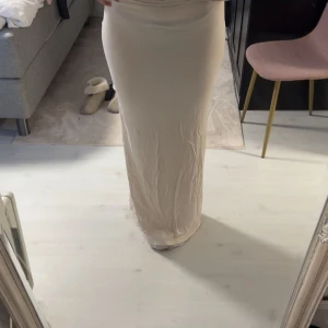 Beige långkjol i stretchigt material - Säljer en beige långkjol med tight passform och hög midja. Kjolen är enkel och stilren, gjord i ett mjukt och stretchigt material som sitter snyggt mot kroppen. Aldrig använd