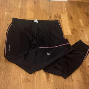 Svarta träningsbyxor Craft XXL - Svarta träningsbyxor från Craft i storlek XXL med rosa sömmar och logga på benet. Byxorna har snörning i midjan och är gjorda i ett lätt och stretchigt syntetmaterial, perfekta för träning eller löpning. Passar dock bra för L 💕