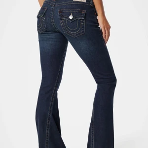 Mörkblå bootcut jeans med fickdetaljer - Snygga mörkblå jeans med bootcut passform och markerade sömmar. Bakfickorna har lock och dekorativa sömmar samt silverfärgade knappar. Jeansen har en klassisk femficksdesign och är perfekta för en trendig look. Slitna på grund av att jag gått på dom ( för jag e för kort ) PRIS KAN DISKUTERAS 