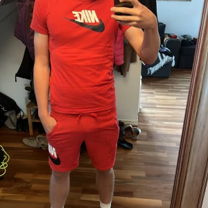 Röda Nike shorts+Tröja med logga - Säljer ett par röda Nike shorts+tröja med stor vit och svart logga på vänster ben. De har snörning i midjan, två sidofickor och är gjorda i mjukt bomullsmaterial. Perfekta för chill eller sportiga dagar, riktigt snygga och bekväma.