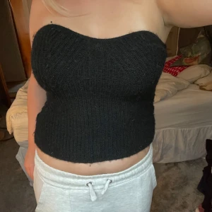 Svart stickad bandeau tubtopp - Säljer en svart stickad bandeau topp. Toppen är ribbstickad och har en croppad passform. Perfekt för dig som vill ha en enkel men trendig look.